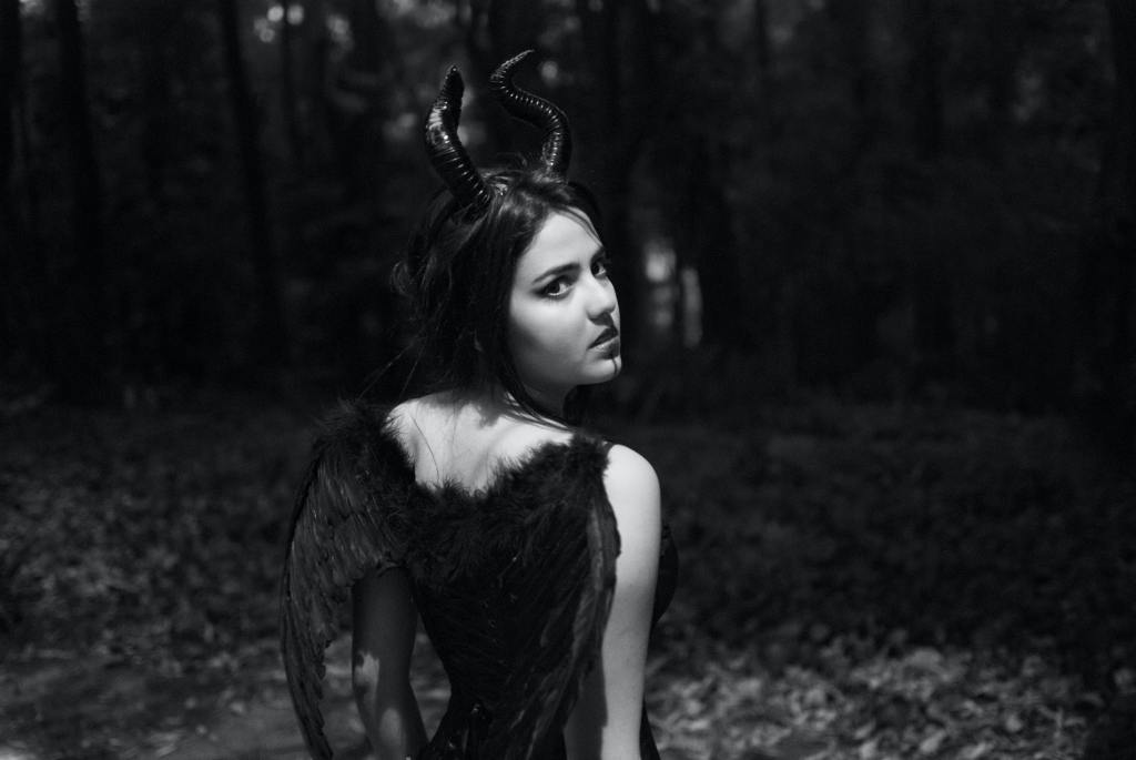 Black and white image of woman with horns and wings in forest. 