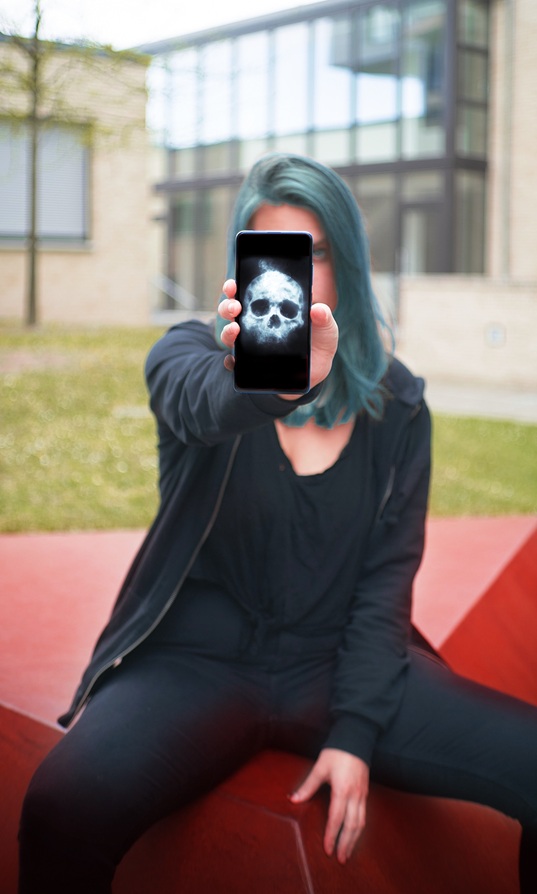 Woman with blue hair holding phone with image of ghostly skull